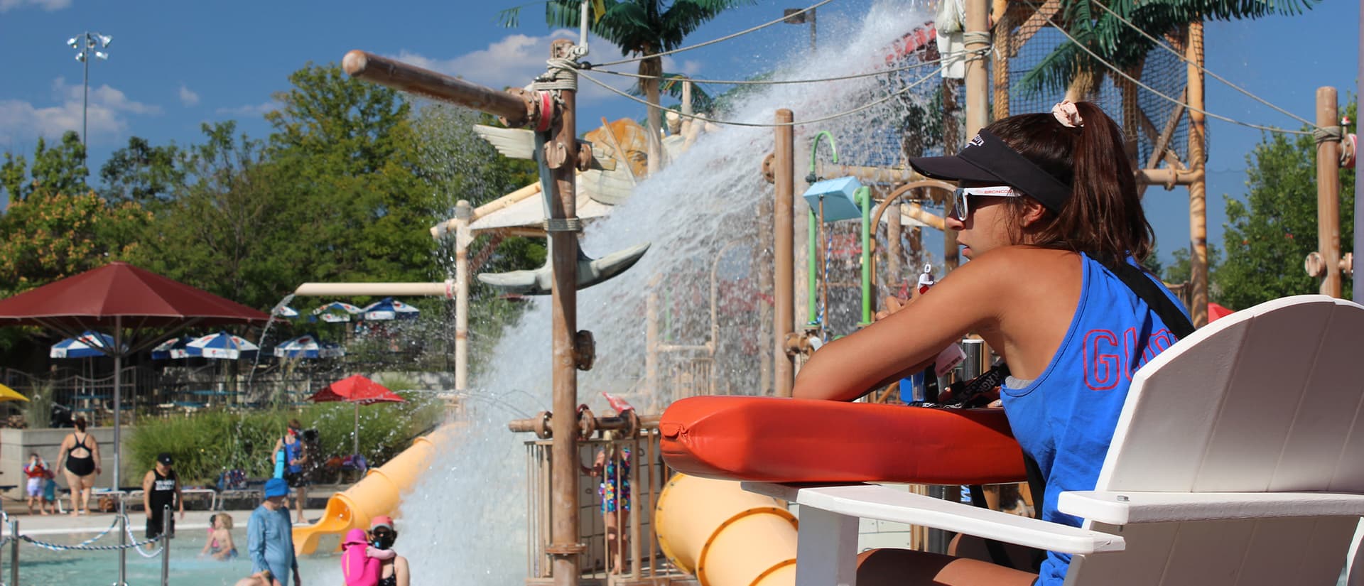 Lifeguard sitting in a chair watching the pool and holding a red rescue tube